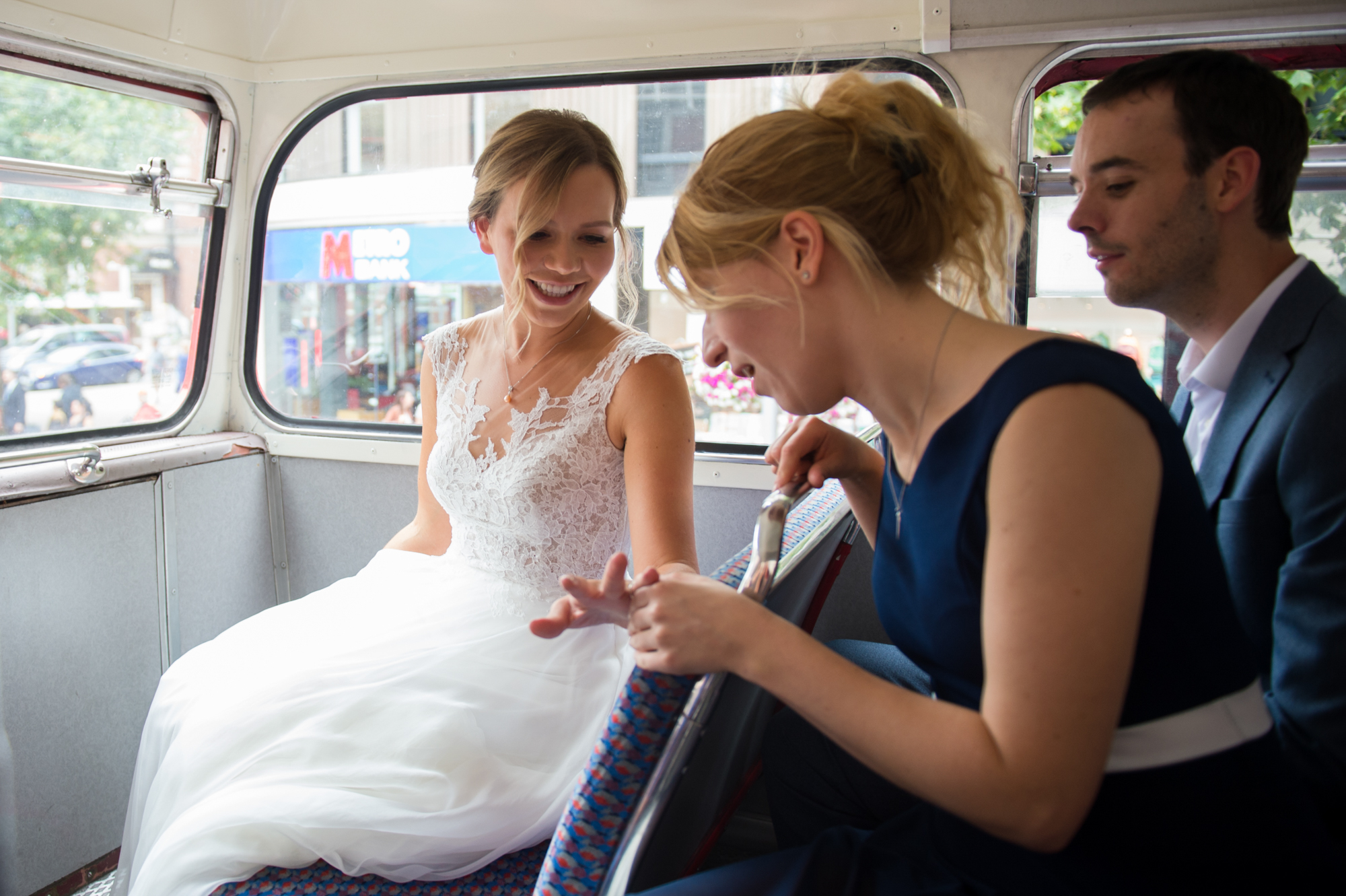 A bride showing her bridesmaid her wedding ring on the top deck of a classic red London bus